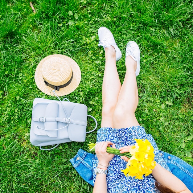 Mulher sentada na grama no parque da cidade com flores amarelas