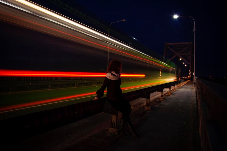 Foto mulher sentada na ponte com trilhas de luz à noite.