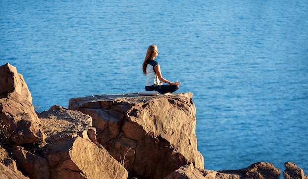 Mulher sentada na posição de lótus na rocha acima do mar e meditando. Yoga ao ar livre