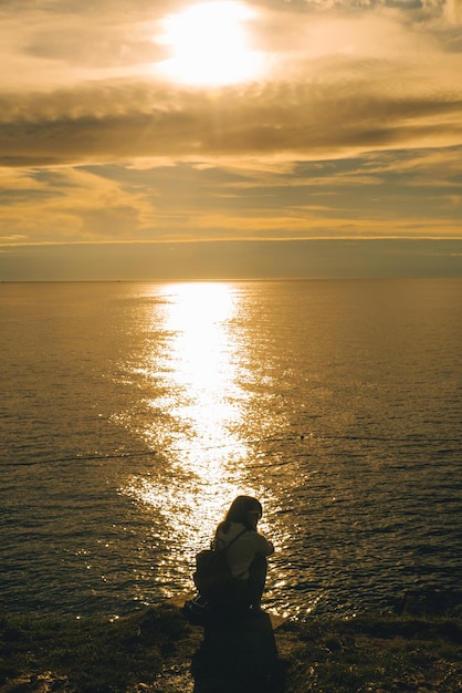 Mulher sentada na praia do mar apreciando a beleza do pôr do sol