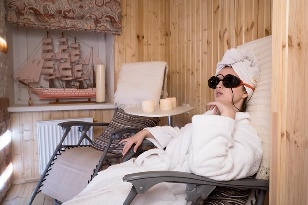 Mulher sentada na sala de terapia de sal e relaxamento ocular usando óculos de terapia de cores digitais