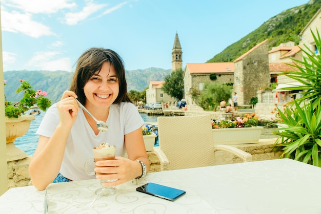 Mulher sentada no café em perast à beira-mar em montenegro comendo sorvete. férias de verão