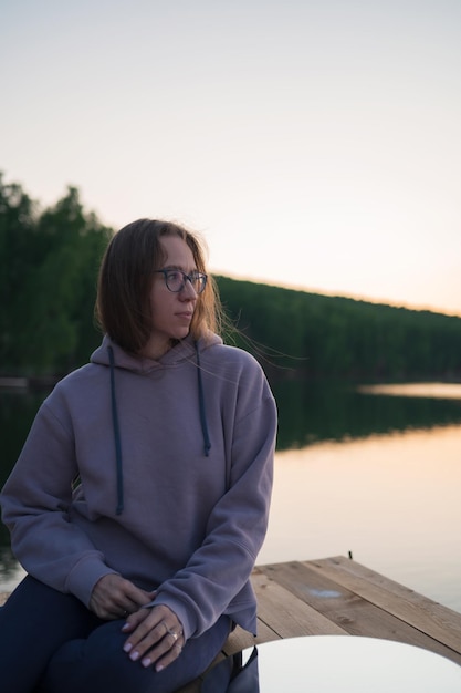 Foto mulher sentada no cais no lago com espelho em círculo no pôr-do-sol de verão