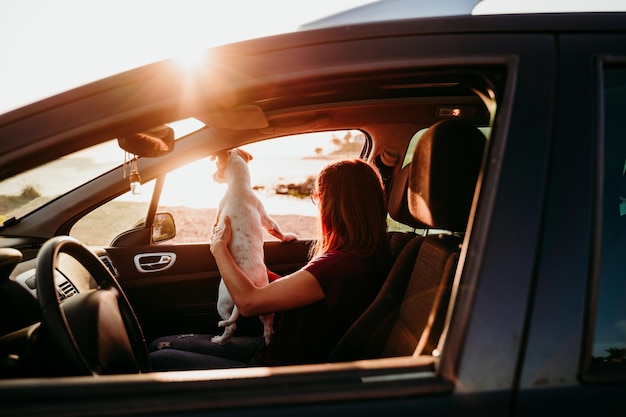 Mulher sentada no carro com o cachorro durante o pôr do sol