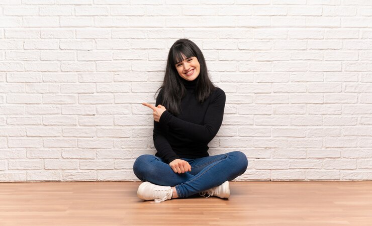 Foto mulher sentada no chão, apontando para o lado para apresentar um produto