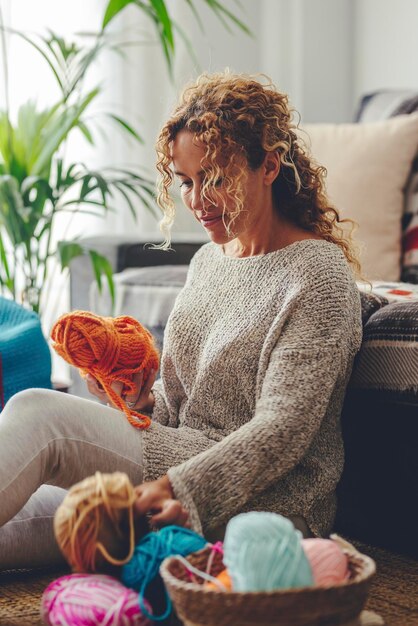 Mulher sentada no chão crocheteando uma bola de lã vermelha criação feita à mão relaxando em uma tarde de domingo conceito de estilo de vida e lazer