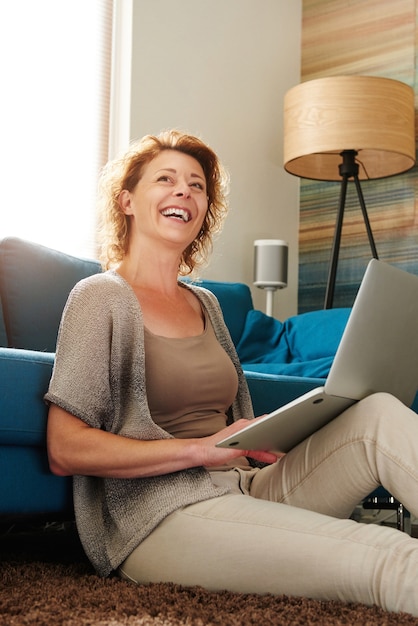 Mulher sentada no chão digitando no laptop rindo