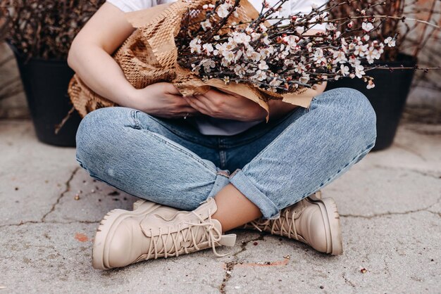 Foto mulher sentada no chão segurando um grande ramo de ramos com flores de cerejeira rosa em flor