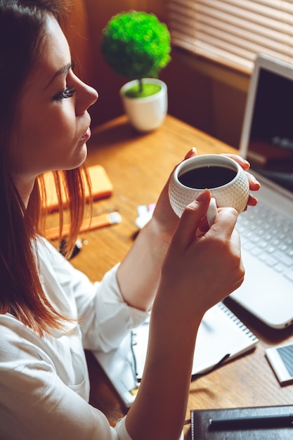 Mulher sentada no escritório em casa com uma xícara de café