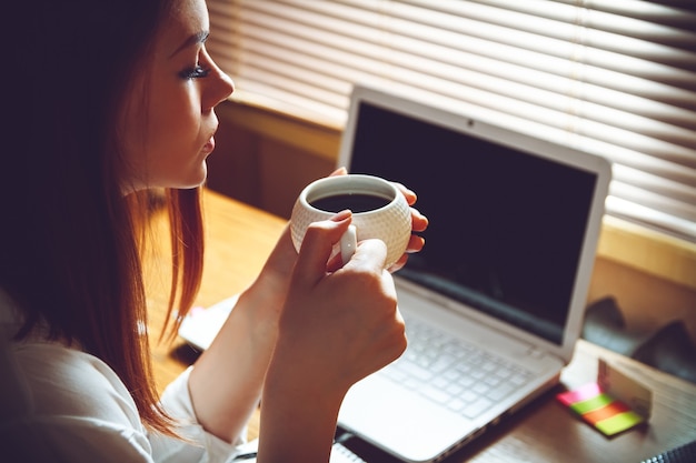 Mulher sentada no escritório em casa com uma xícara de café