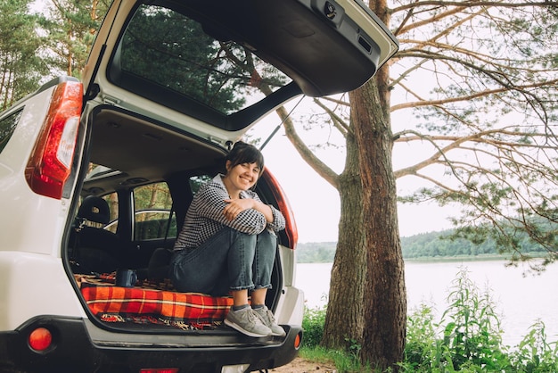 Mulher sentada no porta-malas do SUV conceito de viagem de verão