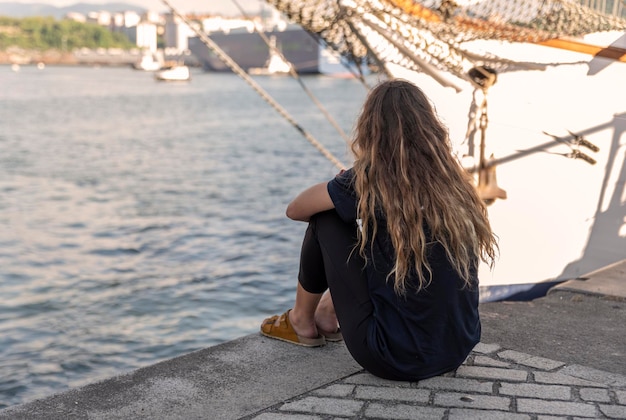Mulher sentada no porto e olhando para o mar