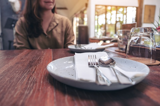 Mulher sentada no restaurante com colher e garfo em um prato na mesa de madeira vintage