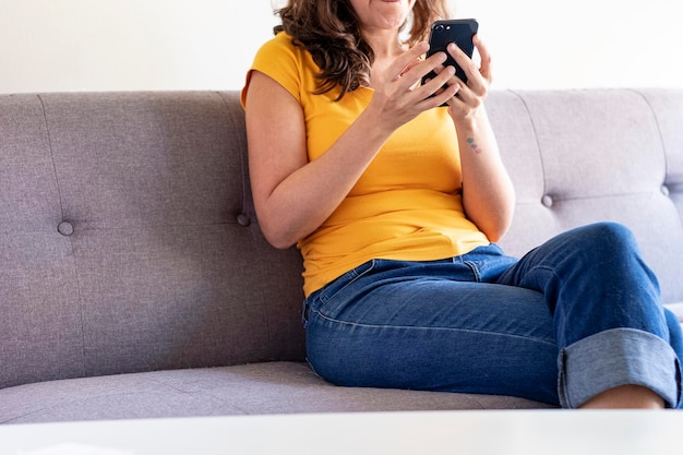 Mulher sentada no sofá com o celular na mão