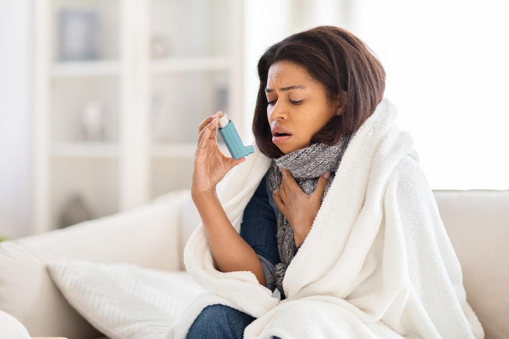 Foto mulher sentada no sofá com um cobertor ao redor usando um inhalador