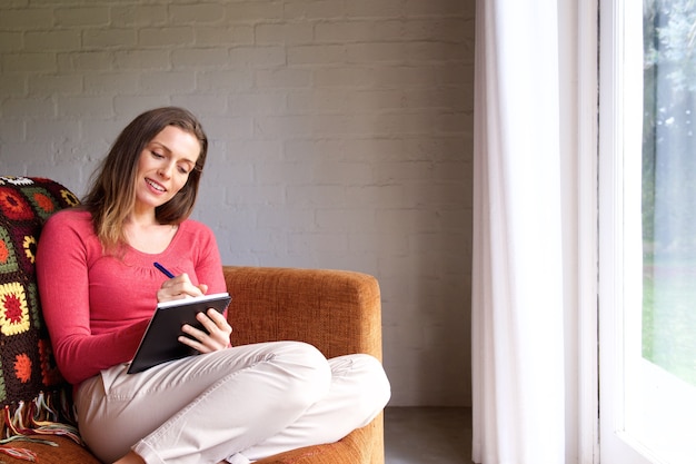 Mulher sentada no sofá em casa e escrevendo no livro
