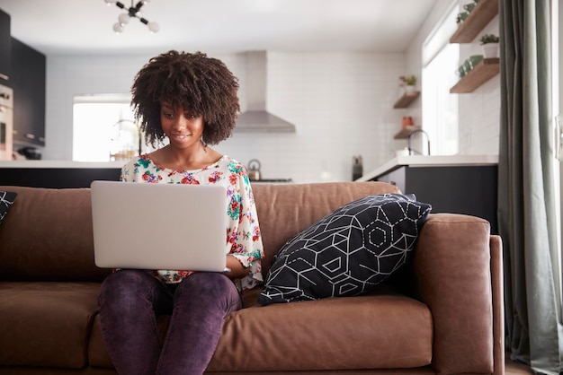 Mulher sentada no sofá em casa usando laptop