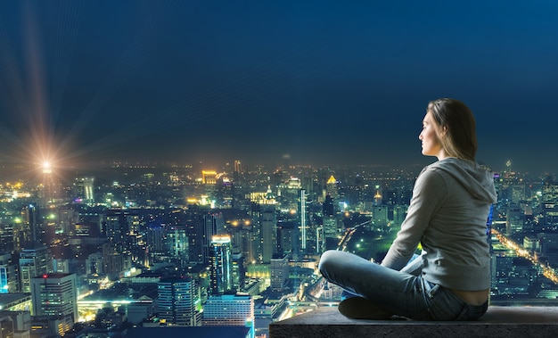 Mulher sentada no telhado com bela vista iluminada da cidade à noite