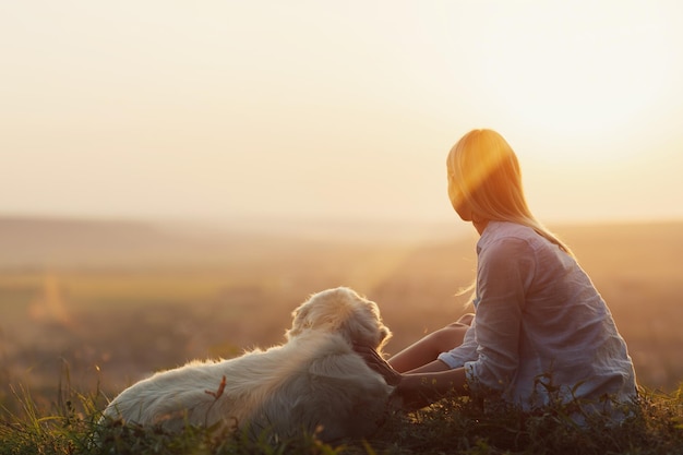 mulher sentada no topo da montanha com cachorro branco e olha para o vale