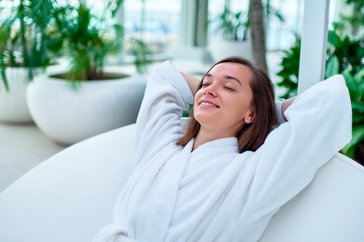 Foto mulher serena e calma vestindo roupão branco, com os olhos fechados e as mãos atrás da cabeça, aproveitando o momento de relaxamento e se sentindo bem em um resort spa de bem-estar.