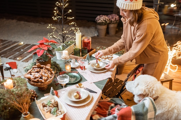 Foto mulher servindo e decorando uma mesa de jantar festiva na véspera de natal ao ar livre no terraço