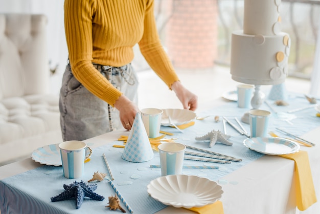 Mulher servindo mesa de festa nas cores azuis com toalha de mesa têxtil, pratos brancos, copos de vinho e talheres de ouro. Feliz aniversário decoração.