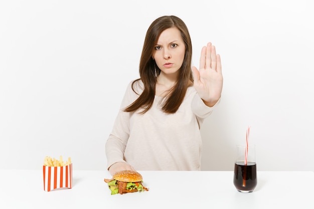 Mulher severa mostra gesto de pare na mesa com cola de batata frita de hambúrguer em frasco de vidro isolado no fundo branco. Nutrição adequada ou fast food clássico americano. Área de publicidade com espaço de cópia.