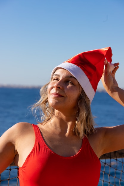 Mulher sexy com chapéu de Papai Noel e maiô vermelho na praia do mar