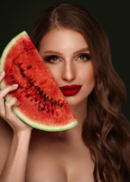 Mulher sexy com maquiagem clássica de cachos e lábios vermelhos segura uma melancia nas mãos Rosto de beleza