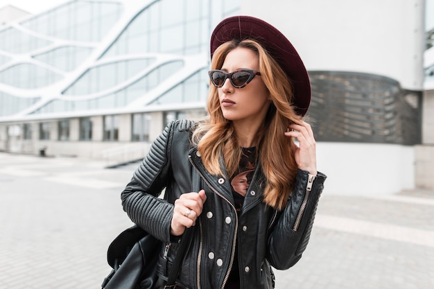 Mulher sexy e moderna hippie com um luxuoso chapéu roxo com uma elegante jaqueta preta e uma mochila com elegantes óculos de sol