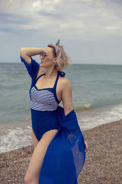 Mulher sexy em um maiô azul e óculos escuros caminhando na praia