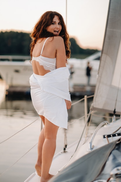 Mulher sexy em uma camisa branca aprecia o pôr do sol em seu iate branco particular