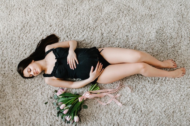 Mulher sexy feliz grávida descansando e deitada no chão ou na cama tocando sua barriga segurando um buquê de flores abraçando a barriga em casa Conceito de maternidade Expectativa de gravidez plana vista superior
