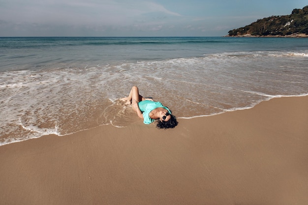 Mulher sexy magro bronzeada de biquíni deitada na costa do mar. Mulher em trajes de praia maiô deitado na areia molhada da praia. Recreação de verão e conceito de viagens.