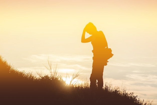 Mulher silhueta com uma bolsa de câmera em um prado ao pôr do sol