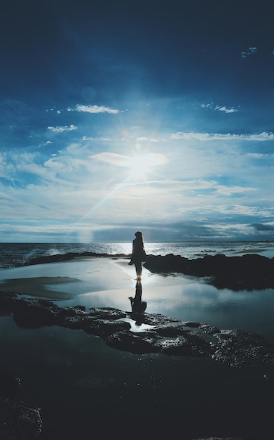 Foto mulher silhueta de pé na praia contra o céu