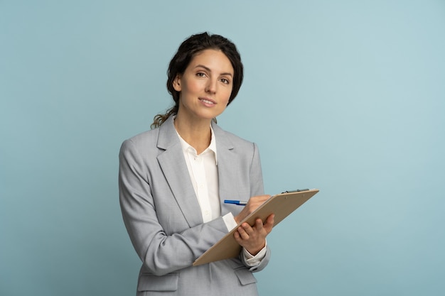 Mulher simpática corretora de seguros usando blazer cinza e blusa branca segurando uma prancheta