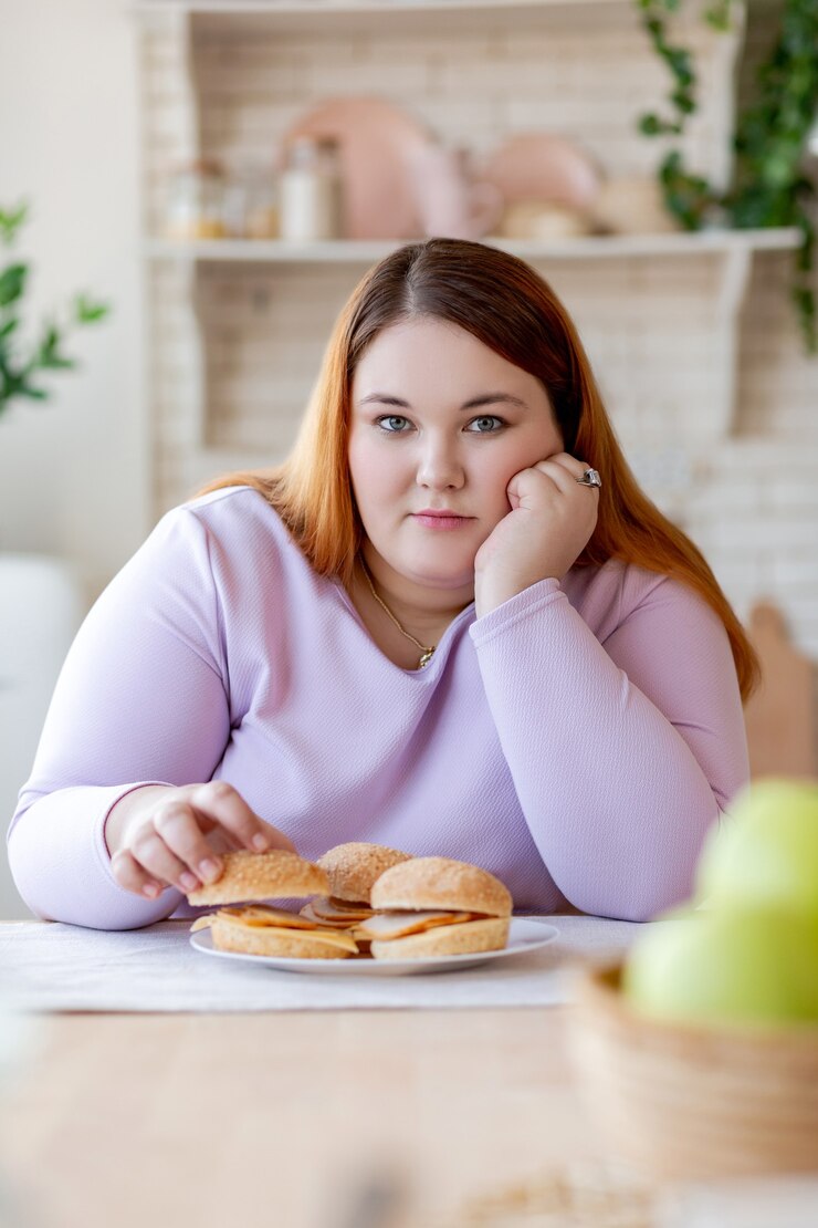 Foto mulher simpática e bonita sentada na cozinha enquanto toma um hambúrguer