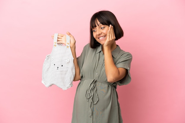 Mulher sobre fundo isolado grávida e segurando roupas de bebê