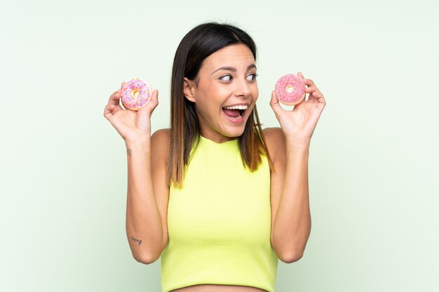 Mulher sobre parede verde isolada segurando rosquinhas e surpreso