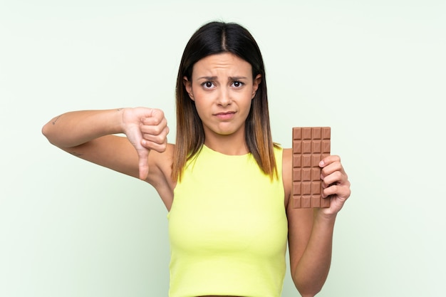 Foto mulher sobre parede verde isolada, tomando um comprimido de chocolate, fazendo sinal ruim