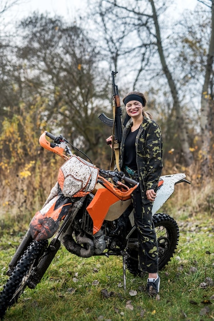 Mulher soldado posando com rifle e motocicleta