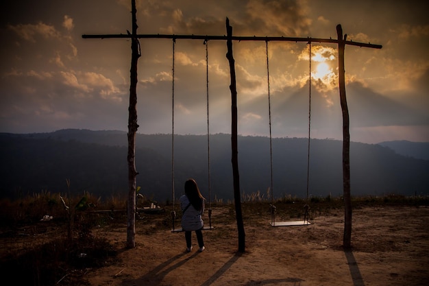 Mulher solitária assistindo o pôr do sol sozinha sentada em balanços na montanha ao pôr do sol