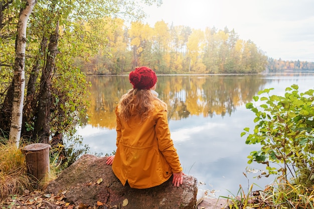 Mulher solitária está sentada na margem de um lago da floresta. Paisagem de outono, calma, tranquilidade, viagens.