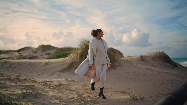 Mulher solteira caminhando na praia de areia nas férias de primavera viajante encaracolado admirando o oceano