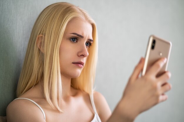 Mulher solteira preocupada olhando para um telefone celular e esperando uma chamada ou mensagem