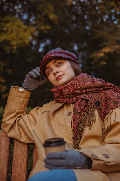 Mulher sonhadora com uma xícara de café relaxante no parque outono ao pôr do sol