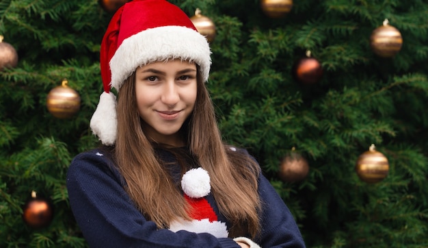 Mulher sonhadora de Natal. Feche o retrato de uma mulher com um chapéu de Papai Noel com emoção. Contra o fundo de uma árvore de Natal