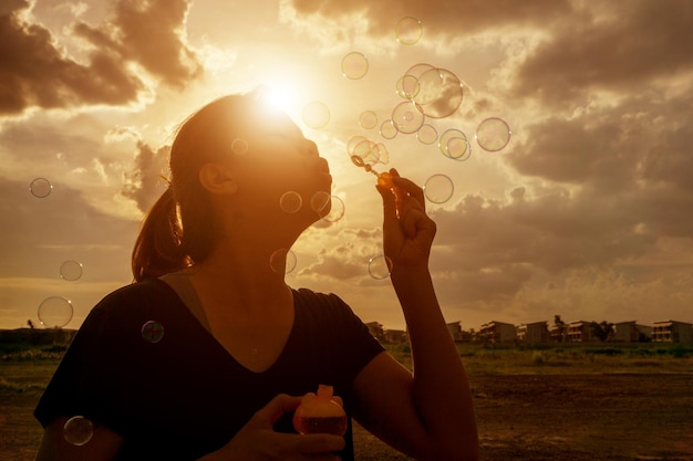 Foto mulher soprando bolhas contra o céu nublado durante o pôr do sol