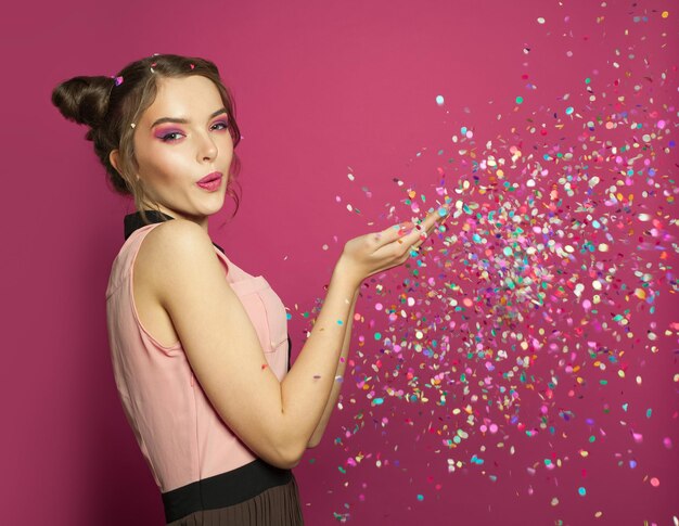 Mulher soprando confete colorido em fundo rosa bonito retrato de modelo de menina feliz